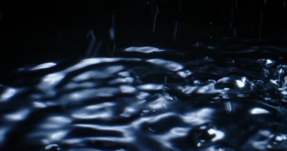 The water surface wavers and begins bubbling with droplets bouncing into the air