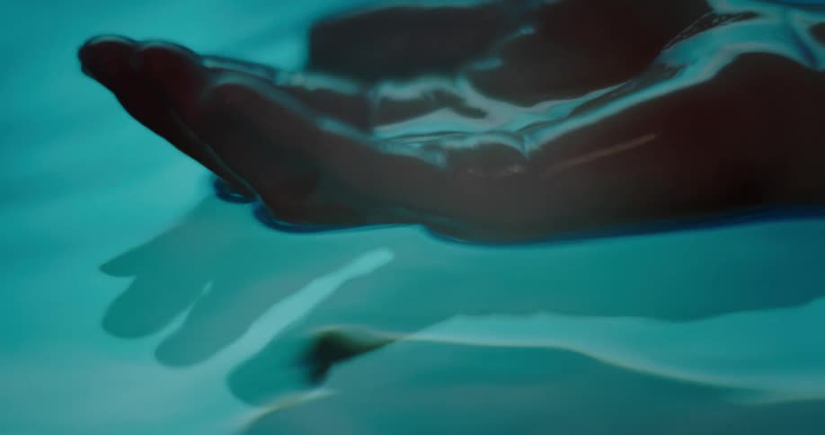 Light shines and reflects on water as it ripples and moves and womans hand slowly rises from underwater