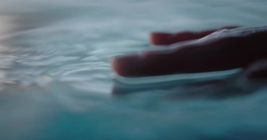 Close up of a hand creating small ripples and waves on the surface of a body of clear water