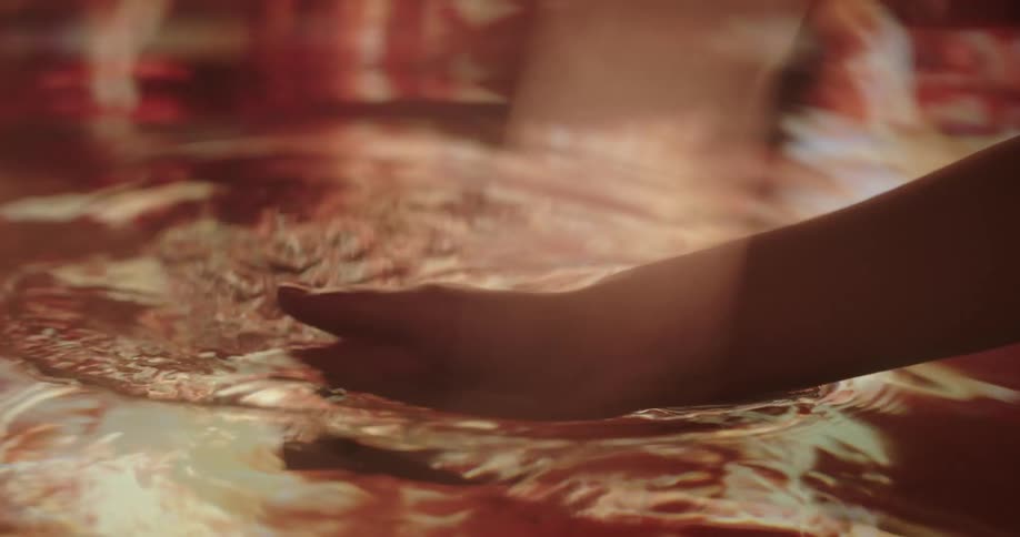 Woman moves hand through water reflecting red and orange light