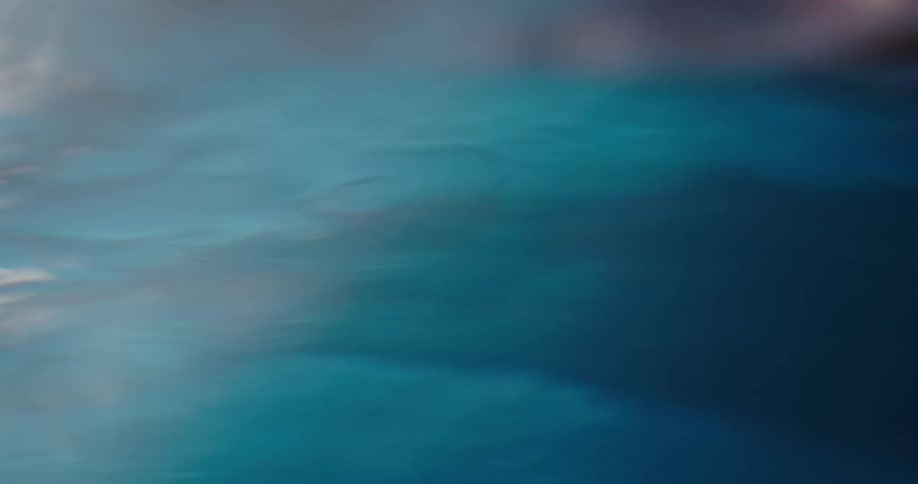 A woman is moving her hand and fingers underwater as light reflects on the ripples