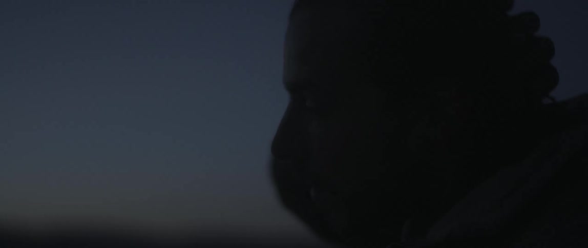 A man is standing outside as it gets dark and he rubs his hand across the top of his head