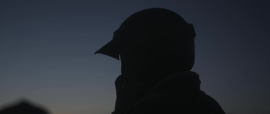 Silhouette of a man putting a cycling helmet on his head and there are mountains in the distance