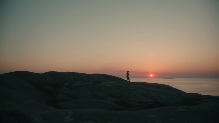 Silhouette of a woman running over a hill next to the ocean at sunset