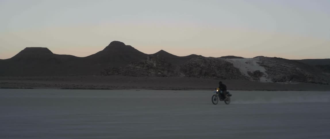 Man with helmet and jacket rides motorcycle at dusk in the desert