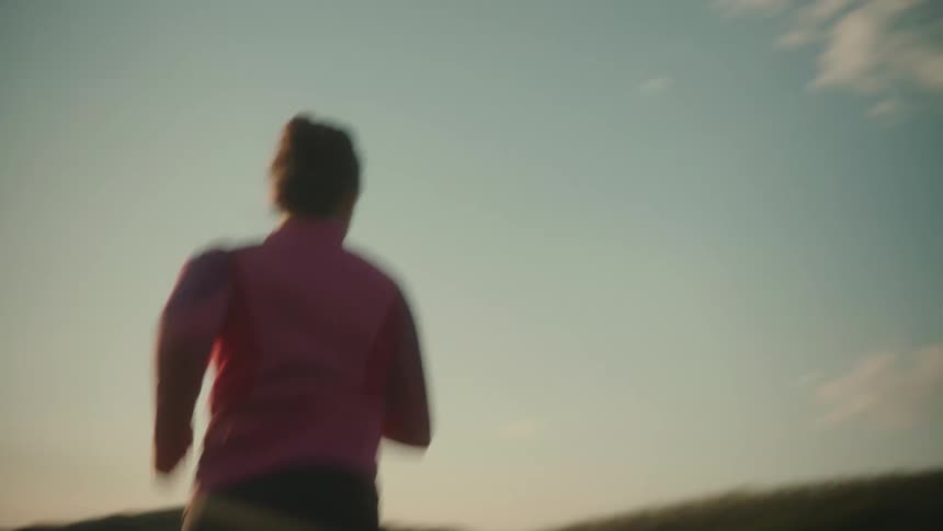 A young woman is jogging with determination in a grassy area