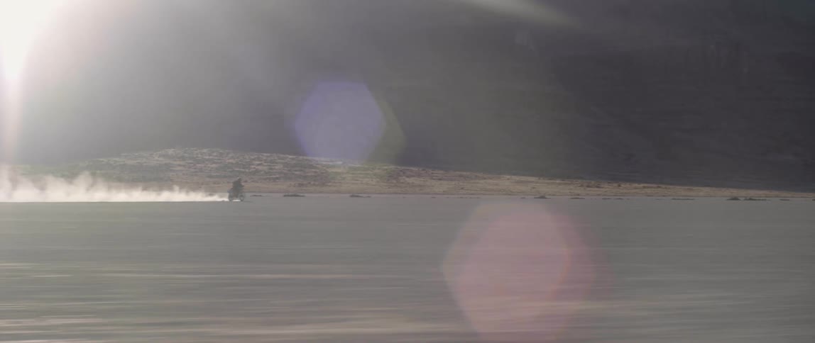 A dirt bike rider driving through the desert kicking up dust in the daylight