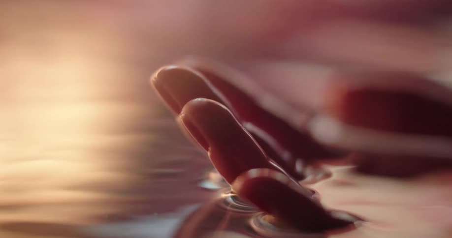 A womans hand is just below the water surface and she moves her fingers as she moves her hand underwater
