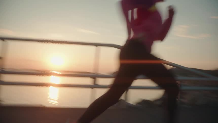 A woman is jogging across a bridge as the sun shines brightly on the horizon