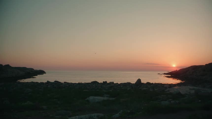 A pink sunset reflecting off the ocean with an alcove beach line