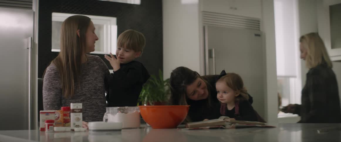 Group of mothers with their kids gather around kitchen island with baking supplies