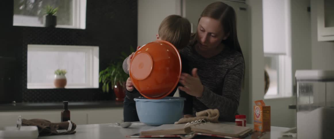 A mother helps her son pour ingredients from a bowl to another