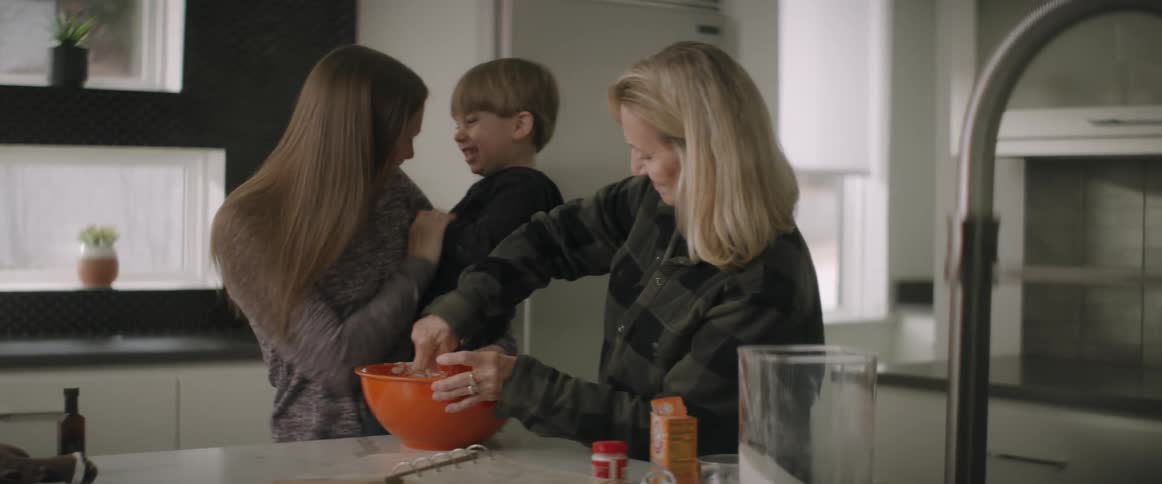 A woman plays with her son while baking with her mother in the kitchen
