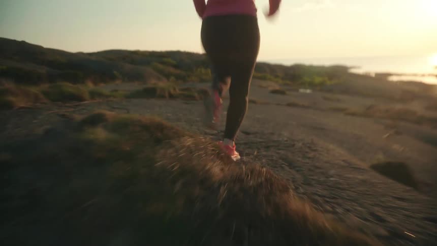 A young woman is jogging along a ridge overlooking the ocean under a sunny sky
