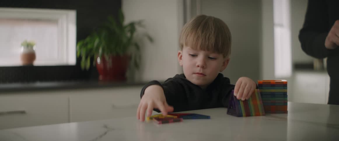A boy pulling triangles off each other and placing them on the counter as an adult stands near