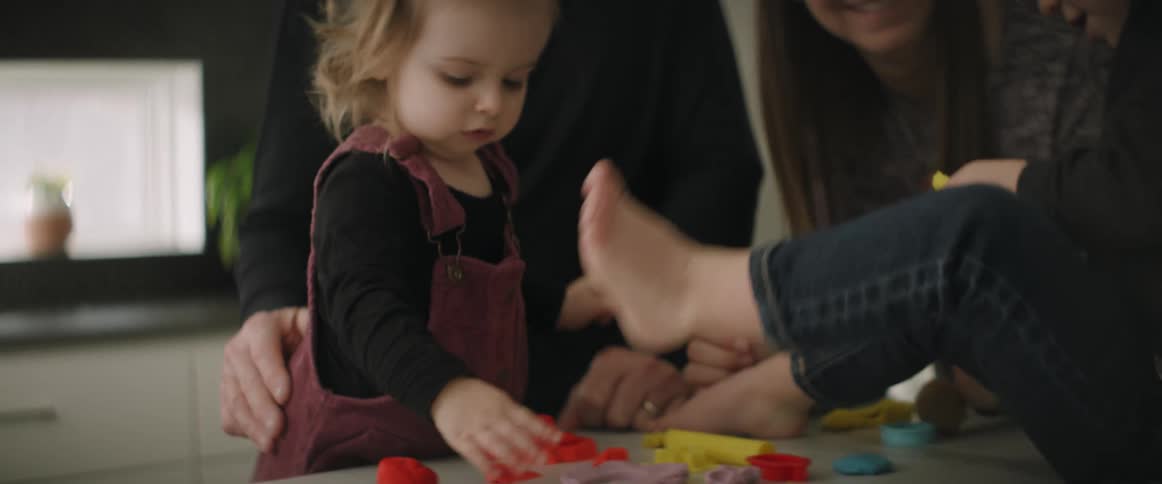 Mom and dad are with their two young children as they play on the table with play dough