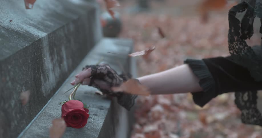 A woman puts a rose on a grave