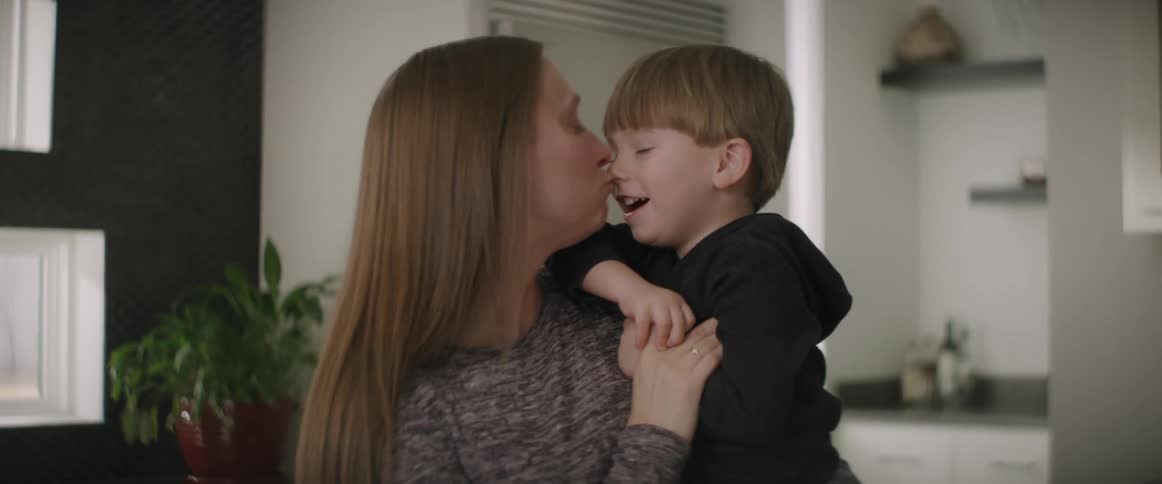 A woman is holding her little boy in her arms and they laugh as she kisses him