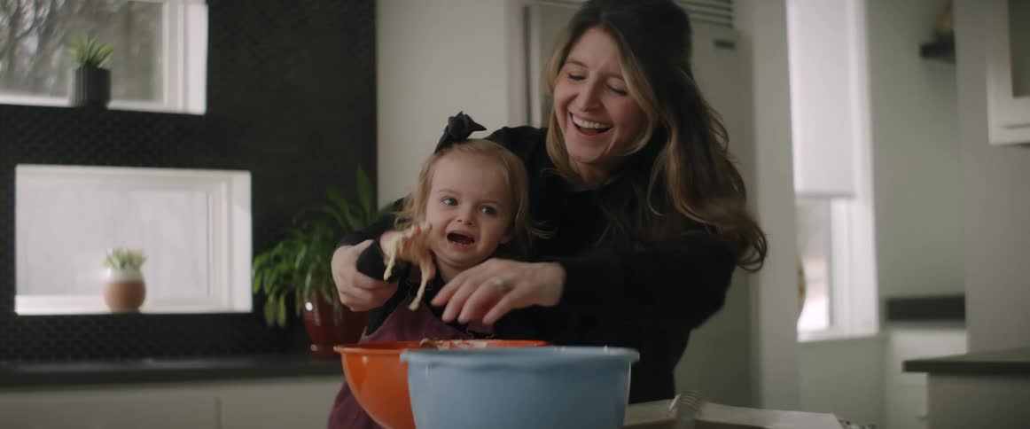 A mother and daughter preparing food as the little girl puts her hand in the mix and starts to cry