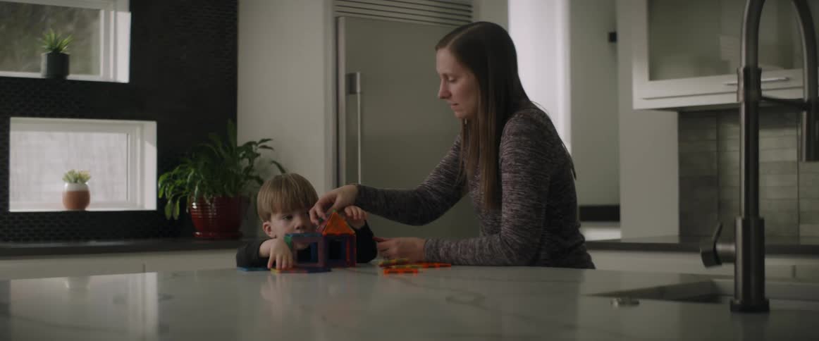 A mother helps her son build a little house with toy pieces