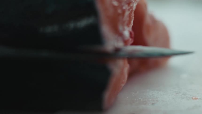 Close up of the hands of a chef using a sharp kitchen knife to slice and cut a fish