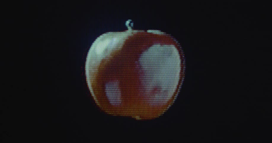 Macro shot of a pixelated rotating red apple floating in and out of focus on flickering retro computer screen with transformation