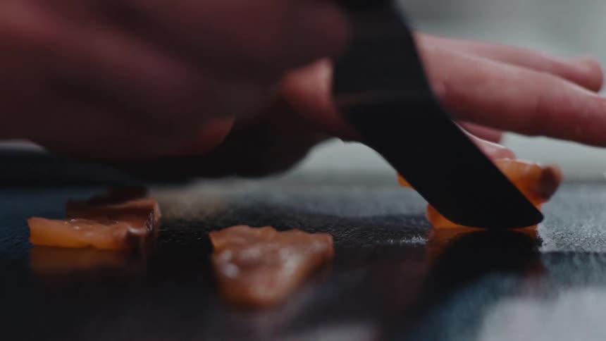 A chef places sashimi cuts of salmon on a plate