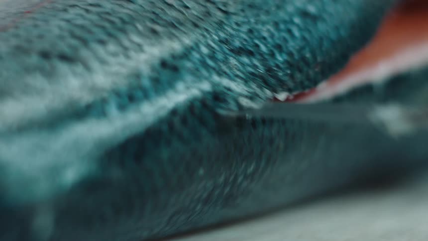 One side of a whole salmon is sliced off with a sharp knife