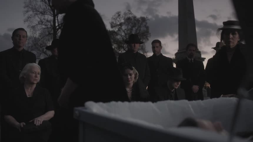 Mourners gather around an open cask in a cemetery