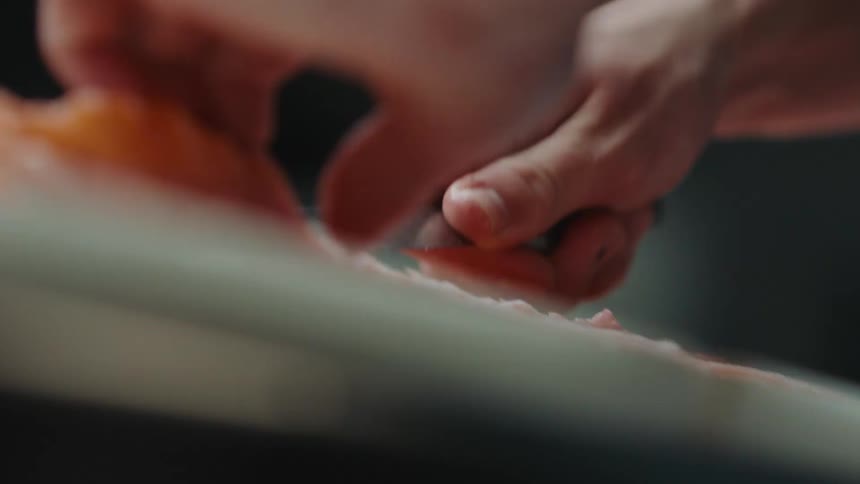 Chef cutting salmon filet off of bone on countertop in kitchen