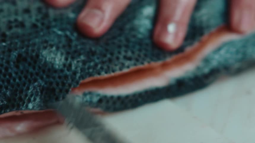 Close up of the hands of a chef using a sharp kitchen knife to slice and cut a fish
