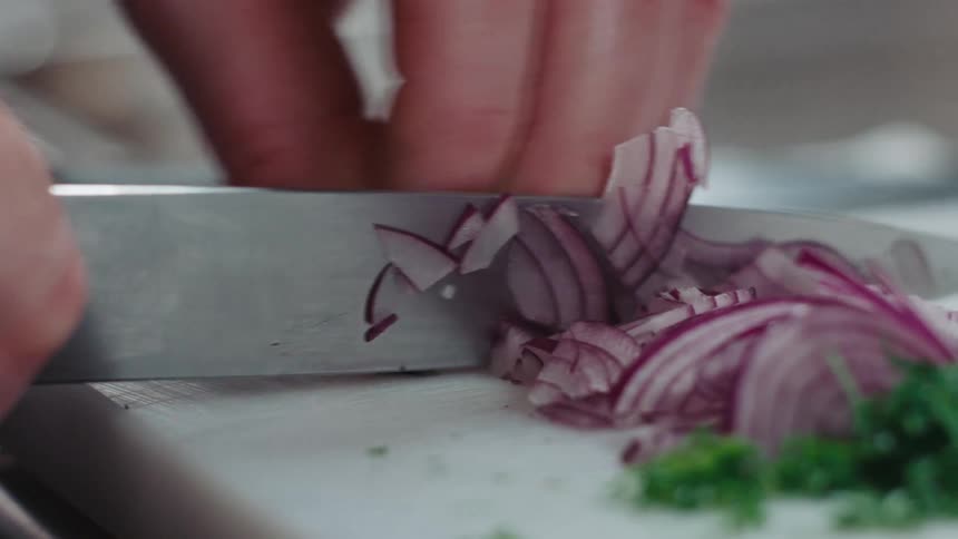 Person rapidly slices red onion on white chopping board