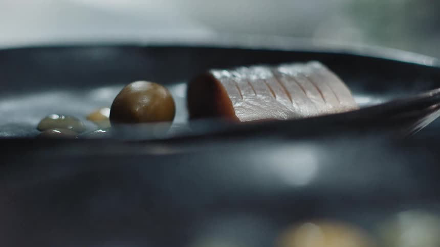 Close up of chefs hand putting an olive in a pan next to salmon steak