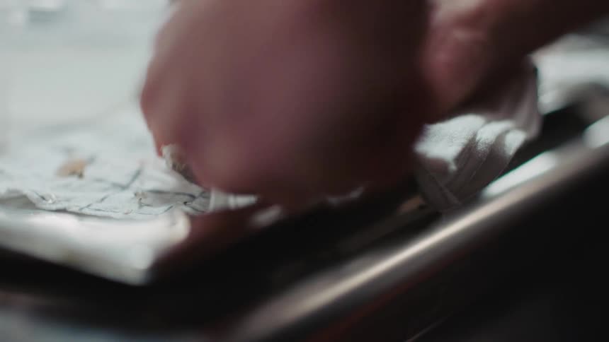 A pair of hands shuck oysters in a stainless steel tray