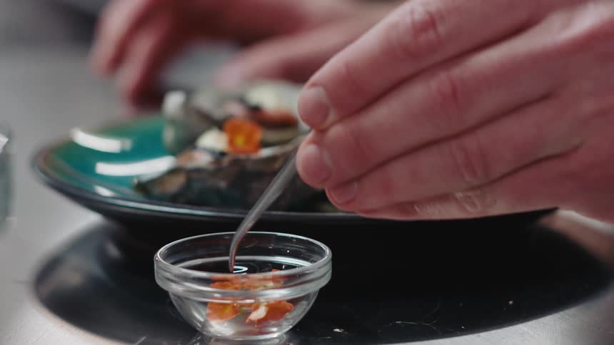 A restaurant cook uses tweezers to place small flowers on top of plated oysters