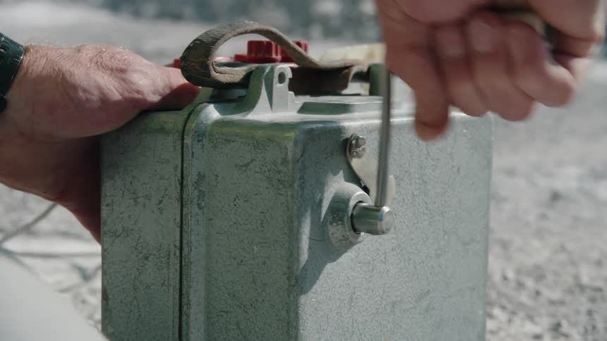 Close up of the hands of a man turning the crank on an old explosives ignition system
