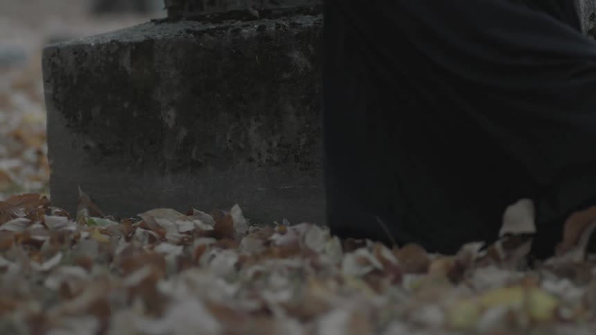 A woman in a black dress walks over leaves