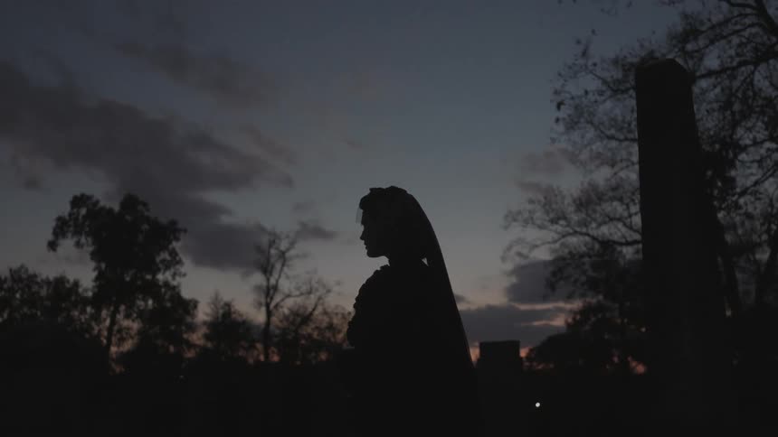 A woman in a cemetery adjusts her veil