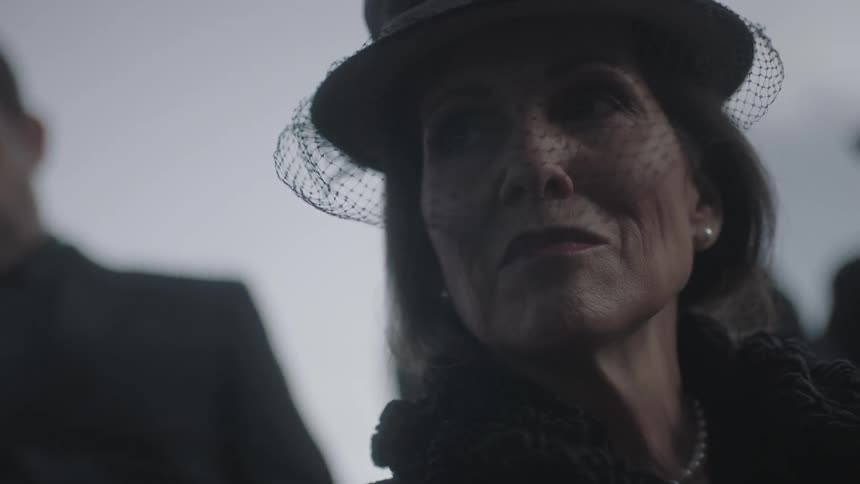 An older woman wearing a black hat looks around