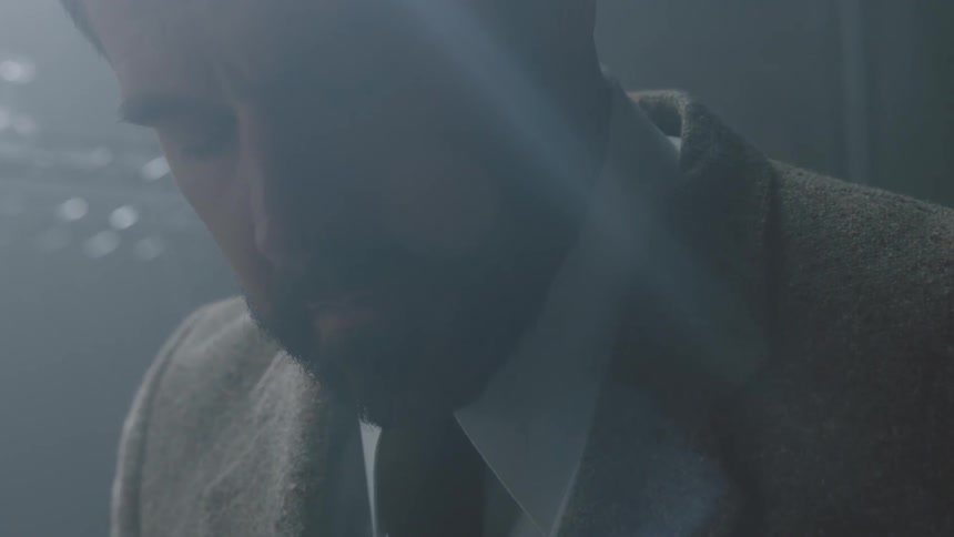 A bearded man in a suit looks down