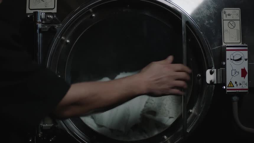 A man closes a commercial sized washing machine with blankets inside