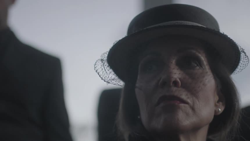 A woman wearing a hat with a veil looks up