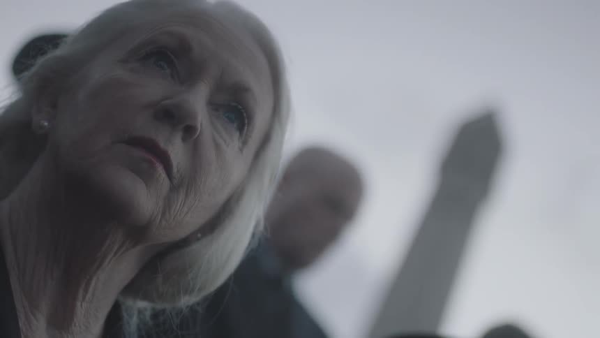 Old woman looks morosely as the sky while several people stand behind her