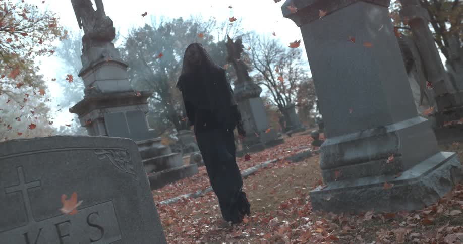 A woman in a black dress walks through a cemetery