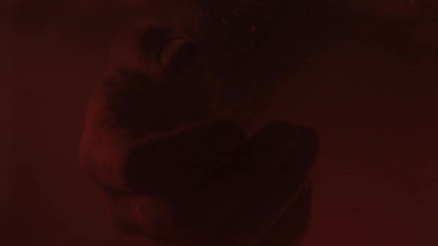 A hand drops into a container of reddish colored water