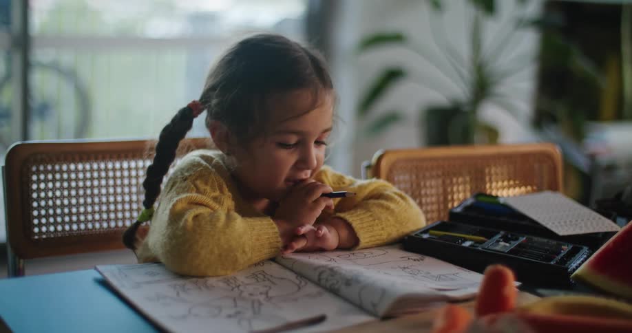 A girl colors in a coloring book while watching her father cut watermelon