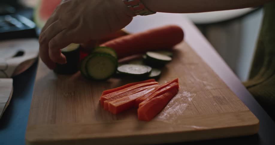 Close up of the hands of a man slicing vegetables over a wooden board with a sharp kitchen knife