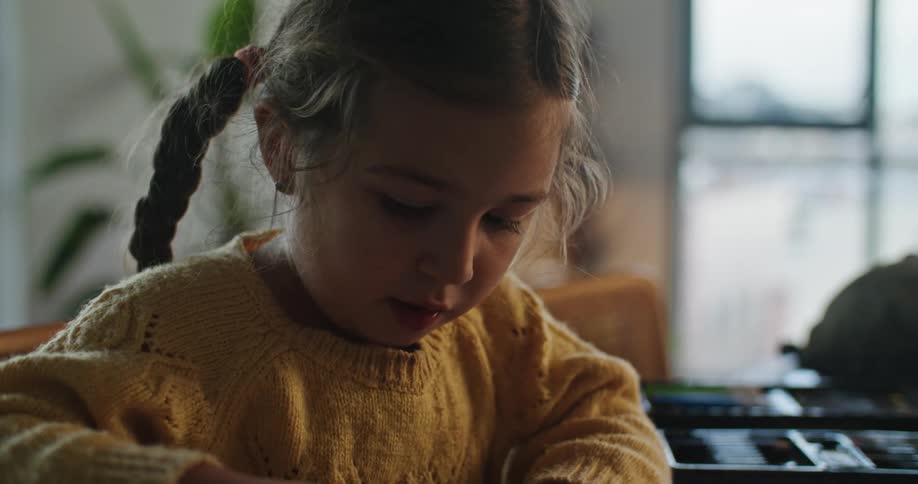 A young girl uses a crayon to color in a coloring book while sitting at a table