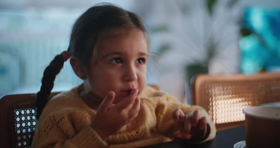 A young girl eats finger foods while sitting at her kitchen counter