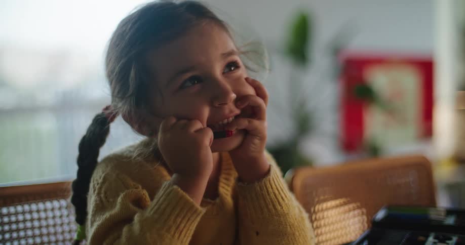 A young girl laughs while sitting in a chair at her kitchen counter